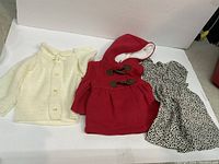 Displays the three baby clothing items: knit cardigan, red hooded jacket, and spotted dress