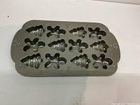 Rectangular metal baking mold with 12 Christmas-themed cavities including gingerbread men, Christmas trees, and candy canes