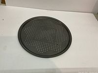 Photo of a round metal baking tray with perforations on the surface to allow airflow during baking.