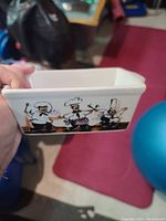 Side view of white rectangular ceramic butter dish featuring cartoon illustration of three chefs in white uniforms cooking and holding kitchen tools.