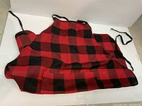 Red and black checkered cooking apron displayed flat on a white surface showing the full pattern and adjustable black strings.