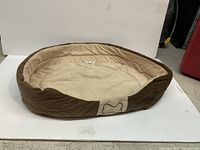 Brown and beige dog bed with raised sides and bone decoration on front.