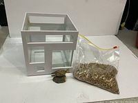 Photo showing a small square glass fish tank with white wooden frame, a resin turtle ornament missing one arm, and a transparent resealable bag full of light brown aquarium gravel.