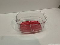 Clear rectangular Tupperware container with side handles and red perforated insert inside, no lid included.