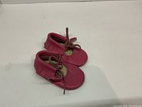 Pink infant moccasins size 2, shown from above on a plain white background.