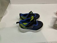 Pair of blue and green Skechers infant running shoes with Velcro straps on a white surface.
