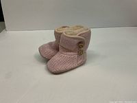 Pair of pink infant UGG boots showing front and side sides, knitted exterior and wooden buttons.