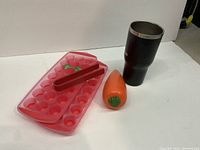 Photo showing two red plastic ice cube trays with lids, red ice tongs, carrot-shaped tupperware, and black travel mug.