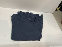 Folded blue men's t-shirt laid flat on white surface.