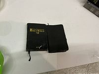 Two mini leather-covered Bibles on white surface, showing front of one with gold text and the second with plain cover.