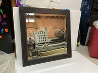 Front view of square wall mirror showing brown leather border and reflective glass surface.