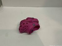 Pair of pink infant Crocs shown folded with heel strap and ventilation holes visible, on white surface.