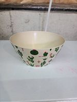 Front angle view of off-white plastic bowl decorated with green cactus and pink flower illustrations around the outside.