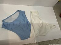 One piece off-the-shoulder bathing suit laid flat showing the front side with a blue and white color-block design.