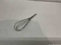 Single metal whisk with balloon wire design and metal handle on a plain white surface.