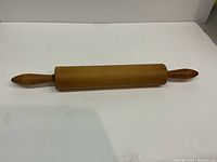Wooden rolling pin with smooth wooden roller and handles at both ends placed on a white surface.