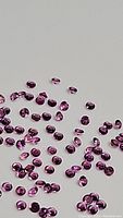 Scattered small round diamond cut pink sapphires on a reflective surface showing color and cut.