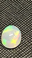Close-up photo of a semi-translucent oval cabochon cut Ethiopian opal showing bright iridescent rainbow colors under light.