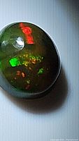 Close-up of oval black Ethiopian opal showing bright red and green flashes on dark body tone.