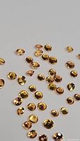 Many small round-cut fanta orange sapphires scattered on a white surface showing their orange color and cut quality.