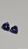 Two deep blue-purple trillion cut tanzanite gemstones shown from above on a neutral background.