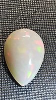 Pear-shaped opal cabochon showing the front with multi-color flashes on a black textured background.