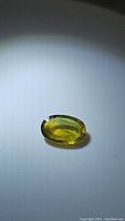 Oval-shaped tricolored sapphire gemstone showing primarily yellow-green coloring with facets reflecting light.