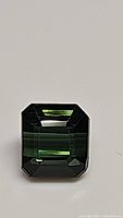 Close-up photo of a natural green tourmaline gemstone, octagon cut, showing facets and clarity.
