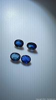 Four oval cut blue sapphires with deep blue color and high clarity resting on a white surface