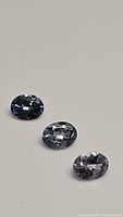 Three oval-shaped natural tanzanite gemstones arranged on a plain surface showing blue-purple color and clarity