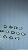 13 pear cut alexandrite gemstones under normal lighting, showing light green to light yellow color.