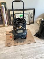 Full view of dark blue Mastercraft air compressor with handlebar, hose coiled on top, and four wheels at base.