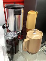 Photo showing four vintage coffee pots and beverage dispensers on glass table.
