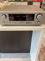 Front view of Denon AV receiver showing control panel, digital display, power button, headphone jack, and input selector knob