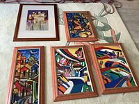 Five framed colorful art prints arranged on a surface showing various abstract and architectural themes.
