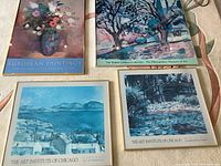 Four framed museum art posters arranged on a patterned surface, showing a floral still life, river scene, blue cityscape, and children playing artwork.