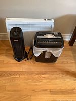 Photo showing Garrison wall heater, Sunbeam tower heater, and paper shredder arranged on floor.