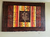 Wide view of large rectangular canvas artwork featuring African-style tribal symbols with texturized raised details and a rustic wooden textured frame.