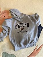 Grey Oxford University hoodie with crest and lettering on front, laid flat