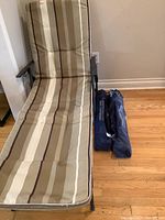 Reclining outdoor lounge chair with brown and beige striped cushion shown from front with two blue camping chair bags on floor beside it.