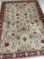 Full view of the rectangular beige Persian style Kerman poly weave area rug with floral and vine design and red border laid on floor.