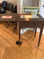 Full view of the sewing machine mounted on a wooden cabinet with fold-out extension and foot pedal on the floor.