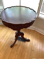 Full view of the round vintage side table showing carved edges and tripod pedestal base with claw feet.