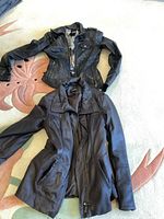 Two black leather jackets laid flat on floor: one biker style and one longer coat style