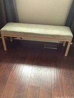 Full view of wooden bedroom bench with upholstered cushioned seat on hardwood floor.