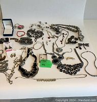 Wide shot showing assortment of jewelry with chains, bracelets, necklaces, rings, brooches including a large black stone necklace and Harley-Davidson ornament.