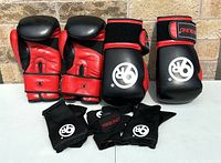 Pair of black and red leather 9 Round boxing gloves positioned upright, showing front and palm side. Accompanied by folded black hand wraps with white 9 Round branding.