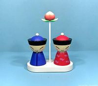 Front view of Mr. and Mrs. Chin salt and pepper shakers on white stand with pink flower topper against blue background.