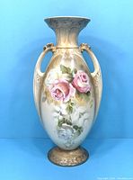 Front angled view of porcelain vase showing floral hand-painted pink and white roses, two handles, and flared rim.