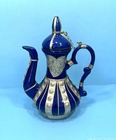 Front angled view of cobalt blue antique teapot with silver floral and band decorations, lid on
